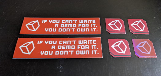 Two small rectangular bumper stickers that say 'If you can’t write a demo for it, you don’t own it' and have a cube on it, and two smaller square stickers with a cube on them