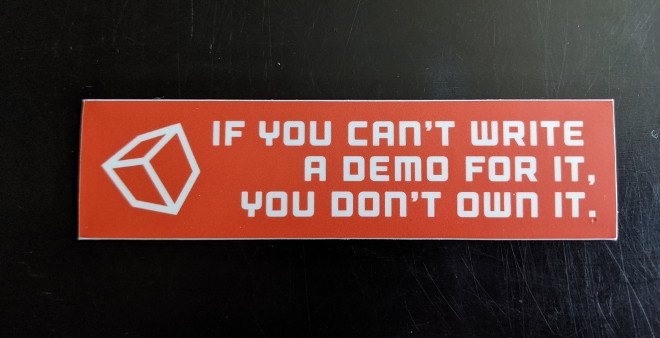 A small rectangular sticker with the text 'If you can’t write a demo for it, you don’t own it' and have a cube on it