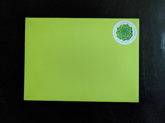 A wasabi-colored envelope with a USPS international forever stamp on it