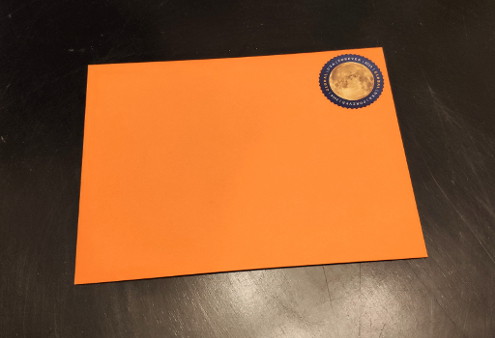 An orange envelope with a USPS international forever stamp on it