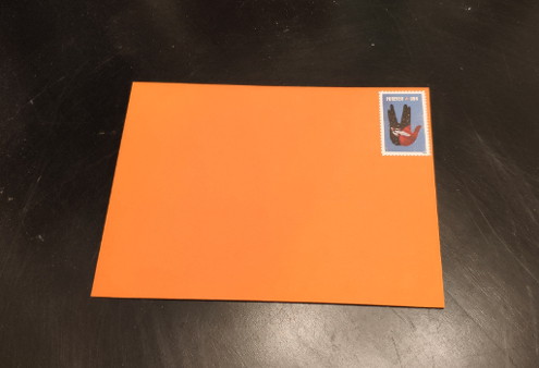 An orange envelope with a USPS domestic forever stamp on it